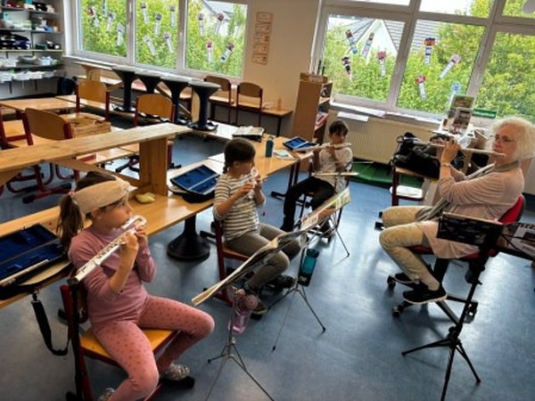 Lehrerin, Schuelerinnen und Schueler spielen Querfloete